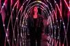 A woman wearing a dark jacket and pants looking up at she walked through a dark tunnel with pink lattice light around her.
