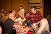 A man in a red and black plaid shirt serving food to a row of guests at the A Christmas Story Dinner Show.