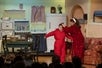 A mother in a red robe putting a hat on a young boy in a red snow suit in a living room on stage at the A Christmas Story Dinner Show.
