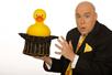 Adam London in a black suit holding a bedazzled hat with a giant rubber duck sticking out of it.