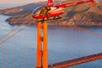 A bright red helicopter flying past the Golden Gate bridge at sun set on the Alcatraz and San Francisco Sites Helicopter Tour.