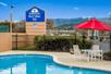 A brigth blue outdoor pool with a table with a red umbrella next to it and a sign for the Americas Best Value Inn in the backgorund.