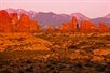 The pink tint of the sunset being cast on all of the arches and rock formations at the Arches National Park with the mountains behind them on the Arches National Park Sunset Discovery Tour Moab Utah.