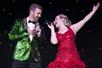Vocalists singing a duet live on stage—one sporting a glimmering green suit coat, the other wearing a beautiful red dress during Array, the exciting new variety show in Pigeon Forge, TN.