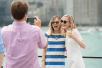 Two blonde women wearing sun glasses posing for a photo near the railing of a cruise boat with New York City in the background.