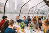 A dining room full of people enjoying their meal next to a glass wall showing the city on the Bateaux New York Premier Brunch Cruise