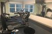 A small fitness center with a couple pieces of cardio equipment and a weights machines in front of a large mirror and a window on the far wall.