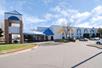 The white and blue exterior of the Baymont by Wyndham Shakopee on a sunny day with cars in the parking lot.