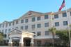 The exterior of the Best Western Plus Valdosta Hotel & Suites with a covered front entrance and trees in the landscaping on a sunny day.