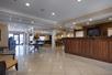 The lobby of the Best Western Plus Valdosta Hotel & Suites with a large dark brown front desk  and a small dining area.