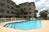 An outdoor swimming pool with light blue water and a few lounge chairs at the far end under a red umbrella on a sunny day at the Best Western Plus Valdosta Hotel & Suites.