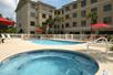 An outdoor hot tub and swimming pool with lounge chairs lining the sides along with red umbrellas and the Best Western Plus Valdosta in the background.