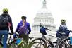 Three tourist wear helmets with bikes and backpacks looking up at United States Capitol Building on an overcast day.