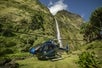 A Helicopter sitting on a clearing in front of a waterfall and cliff on the Big Island Spectacular Helicopter Tour in Hawaii USA.