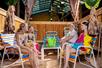A group of four smiling teenagers sitting in colorful chairs in a large bamboo cabana at the Big Kahuna's Water Park.