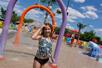 A young girl playing in arched sprinklers in the outdoor kiddie area on a sunny day at Big Kahuna's Water Park.