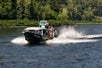 The Explorer Jetboat full of tourists in motion with water splashing around it and trees in the background.