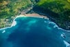A small cove with blue ocean water crashing against the beach and rocks on the Blue Skies of Oahu Helicopter Tour in Hawaii USA.