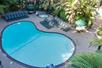 Aerial view of a small shaded outdoor pool surrounded by lounge chair and lush green landscaping.