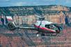 A silver and black Maverick Airbus helicopter flying over the Dragon Corridor of the Grand Canyon on a sunny day.
