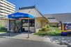 The front exterior of the Comfort Inn Denver Central with beige stone walls, sliding glass front doors and a bright blue awning over the entrance on a sunny day.