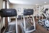 A small fitness center with a window, two treadmills, an elliptical, a free weights section, and a weights machine.