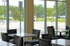 A dining area with square tables with gray chairs and large windows showing landscaping and the parking lot.