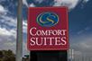 Close up of the red and blue sign for the Comfort Suites New Braunfels on a sunny day with clouds in the sky overhead.