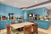 A breakfast area with blue walls and cabinets and an assortment of food options with a table and chairs in front of it.