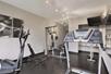 A small fitness center with a few different work out machines, a large mirror, and a television mounted in the corner.