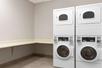 A hotel guest laundry area with two stacked sets of white washers and dryers with a built in folding area to the left.