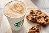 A hot Starbucks beverage with foam on the top and a chocolate chip cookie broken in half on a plate.