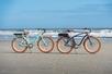 Two bikes with brown tires parked on a beach with waves crashing behind them.