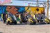 Three yellow GoCars with tourists in them lined up in front of a brightly colored mural on a sunny day in Las Vegas.