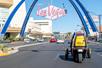 View of a yellow GoCar from behind driving dow the Las Vegas strip with other cars around it on a bright and sunny day.