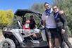 Two young boys sitting in a silver ATV with their parents standing at the front, all smiling, on a sunny day with Desert Dog Off Road Adventures.