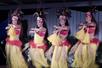 Hula dancers in red and yellow traditional costumes on stage performing at Diamond Head Luau on Oahu.
