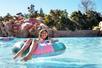 A young girl floating in a pink, green, & blue tube with a waterslide in the background at Disney's Blizzard Beach in Orlando, Florida, USA.