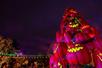 A tower of jack o'lanterns with green glowing faces at night with string lights behind them at Dollywood in Pigeon Forge, Tennessee, USA.