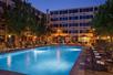 A bright blue outdoor swimming pool with lounge chairs lining the sides along with small trees at night with the DoubleTree By Hilton in the background.
