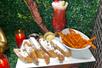 Chicken and waffles dusted with powered sugar on a white plate with sweet potato fries and a red cocktail with whipped cream.