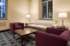 A sitting area with a beige couch, two maroon chairs, a wooden coffee table, and two side tables with lamps.