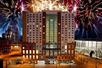 The front exterior of the Embassy Suites by Hilton Denver Downtown Convention Center at night with fireworks going off behind it.