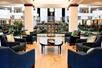A large hotel lobby with tons of green plants, several circular light fixtures, and a sitting area with blue accent chairs and a round coffee table,