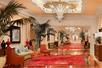 An elegant common area decorated in red and gold with a sofas, chairs, carpets, plants, and exquisite lighting fixtures.
