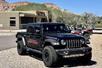 A black Jeep Gladiator park in gravel with red and silver ATVs behind it on a sunny day in Zion National Park.