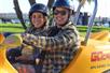 A man and woman smiling and wearing black helmets while sitting in a GoCar on a sunny day on the Experience San Diego GoCar Tour.