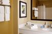 A private bathroom with yellow walls, a white vanity with toiletries on it, a large mirror, and a shower.