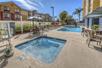 An outdoor swimming pool and hot tub with lounge chairs and tables with umbrellas on the sides on a sunny day at the Fairfield Inn & Suites.