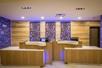 Two light brown front desks with white counters with wooden cut out art on the wall behind them and purple light illuminating it.